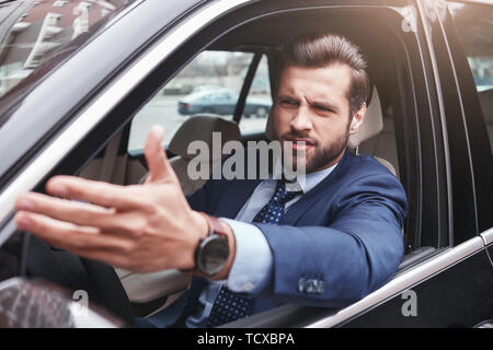 Non mi piace. Arrabbiato ed emotivo di imprenditore nel formale di usura è gesticolando e facendo una grimace mentre alla guida della sua auto. Le emozioni negative. Business c Foto Stock