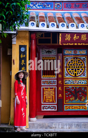 Un giovane vietnamita donna che indossa un tradizionale Ao Dai vestire e di stare al di fuori di un tempio nel centro storico della città, Hoi An, Vietnam, Indocina, Sou Foto Stock