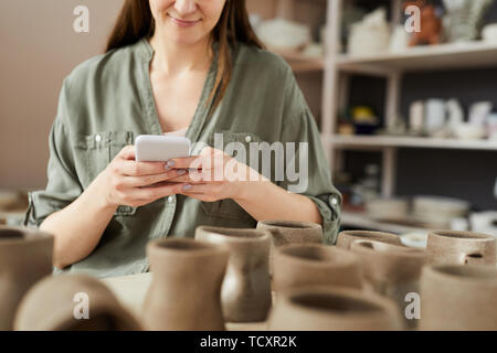 La sezione centrale verticale del contemporaneo artisn utilizza lo smartphone mentre si lavora in ceramica shoip, spazio di copia Foto Stock