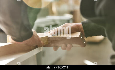 Close up di carpenter con le mani in mano la lucidatura di tavola di legno tramite carta vetrata in officina. Inquadratura orizzontale Foto Stock