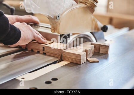 Immagine ritagliata delle mani di un artigiano il taglio di una trave di legno con una sega circolare in un workshop Foto Stock