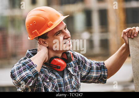 Prestare attenzione a. Operaio edile nel casco protettivo sensazione di dolore al collo mentre si lavora al sito in costruzione. La costruzione dell'edificio. Il concetto di dolore. Pericolo Foto Stock