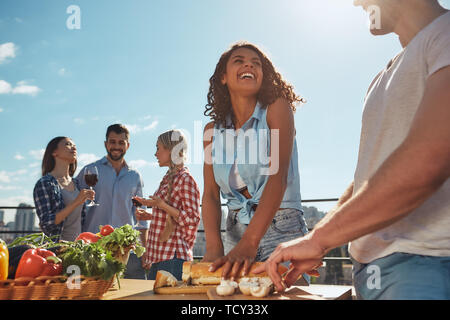Picnic estivo. Due giovani e allegri amici in abiti casual preparare il cibo per il barbecue party e sorridenti mentre si sta in piedi sul tetto. Avendo divertimento. Foto Stock