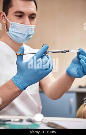 Medico maschio con iniezione. Giovane odontoiatra prepara una siringa per iniezione. Il trattamento dentale. Focus sulla siringa. Colpo verticale Foto Stock