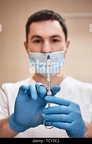 Medico maschio con iniezione. Giovane odontoiatra prepara una siringa per iniezione. Il trattamento dentale. Focus sulla siringa. Colpo verticale Foto Stock