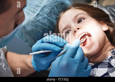 Close-up di bambina apre la sua bocca ampia in fase di ispezione del cavo orale. Dentista è a controllare i suoi denti utilizzando strumenti dentali. Medicina e hea Foto Stock