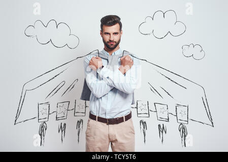 Vorrei proteggere voi. Giovane uomo barbuto che indossa una disegnata battenti capo azienda il pugno vicino al petto mentre in piedi contro uno sfondo grigio con illustratio Foto Stock
