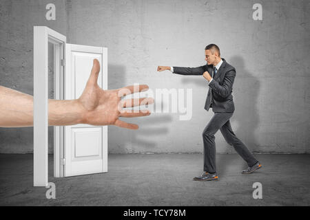 Grandi ragazzi mano aperta che appare attraverso la porta bianca e imprenditore, rendendo la calciata gesto sul muro grigio sfondo Foto Stock