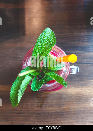 Immagine della vista dall'alto in basso drink rosso con verde menta e paglia giallo su sfondo di legno Foto Stock