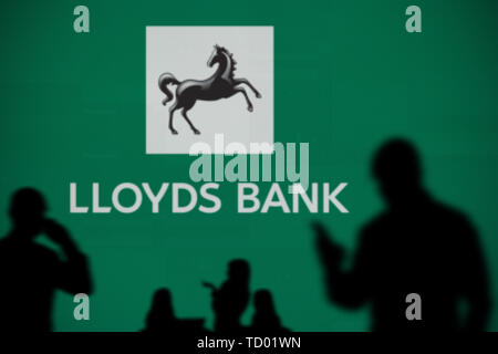 La Lloyds Bank logo è visibile su uno schermo a LED in background mentre si profila una persona utilizza uno smartphone in primo piano (solo uso editoriale) Foto Stock