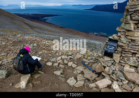 Escursionismo donna scrivi nota in montagne log book, Svalbard paesaggio di montagna, vista da sopra a Longyearbyen Adventdalen fiordo Isfjord e alla fine di un Foto Stock