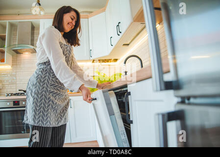 Giovane donna graziosa mettere i piatti in lavastoviglie Foto Stock