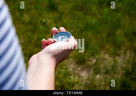 Giovane donna in possesso di una bussola magnetica in mano e stai cercando il modo. Fuori fuoco prato con sfondo di erba. Foto Stock