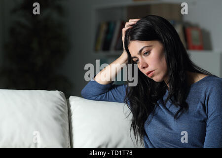 Donna triste pensare che guarda lontano seduto su un divano nella notte a casa Foto Stock