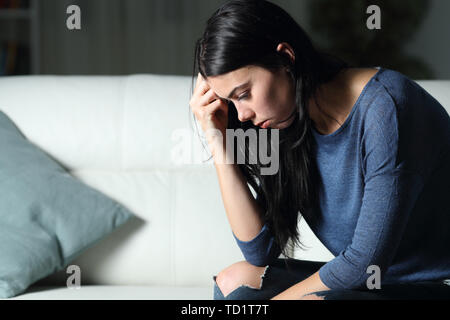 Donna preoccupati pensando da sola seduta su un divano nella notte a casa Foto Stock