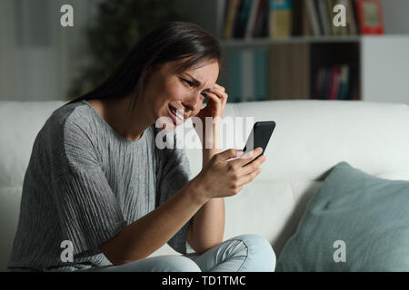 Triste donna controllo smart phone nella notte seduto su un divano nel salotto di casa Foto Stock