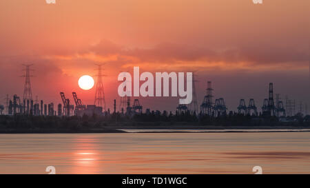 Riverbank con sagome di terminal per container gru durante un colore rosso del tramonto, porto di Anversa, Belgio. Foto Stock