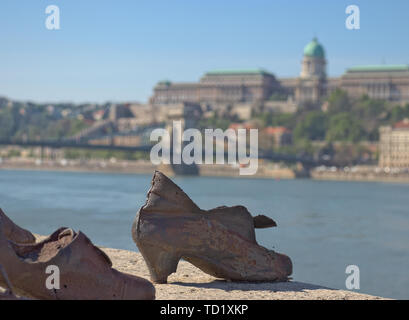 Budapest, Aprile 2019: Le scarpe memorial sulla banca del fiume del Danubio con il ponte delle catene e Palazzo reale in background. Foto Stock