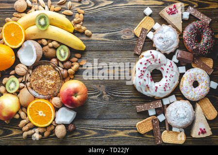 Malsano e dolci sani su sfondo di legno. Organici e prodotti alimentari dietetici e il problema del rifiuto da dessert nocivi. Frutta e noci vs ciambella Foto Stock