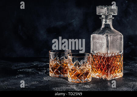 Bicchieri di whiskey con un decantatore quadrato su una pietra nera dello sfondo. Foto Stock
