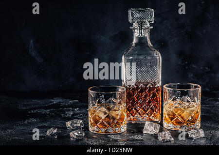 Bicchieri di whiskey con un decantatore quadrato su una pietra nera dello sfondo. Foto Stock