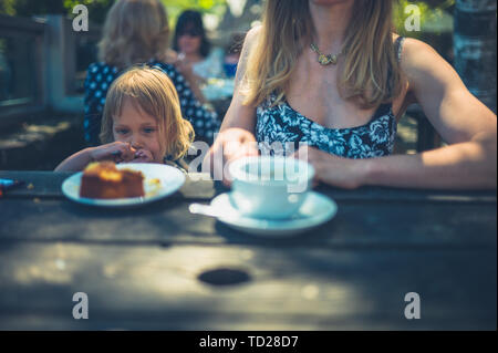 Una giovane madre e il suo bambino sono un caffè e torta presso un cafè all'aperto in estate Foto Stock