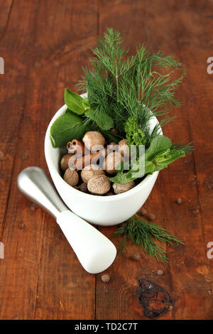 Le erbe e le spezie nel mortaio di ceramica, su sfondo di legno Foto Stock