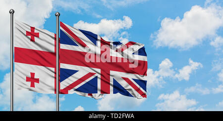 La Georgia e Regno Unito bandiera sventolare nel vento contro bianco torbido cielo blu insieme. Concetto di Diplomazia e relazioni internazionali. Foto Stock