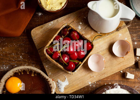 Elevato angolo di visione degli ingredienti per preparare una coca de cireres, una ciliegia dolce torta piatto tipico della Catalogna, Spagna, come ad esempio farina di grano, latte, suga Foto Stock