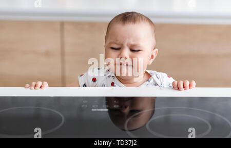 Baby boy raggiungendo alla calda stufa elettrica Foto Stock