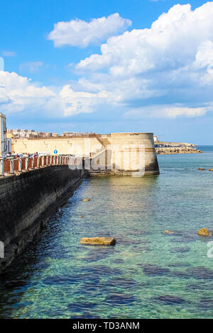 Immagine verticale del mare trasparente e vicina città della costa siciliana di Siracusa, Italia. Presa vicino al centro storico di Isola di Ortigia. Giornata di sole e cielo blu con nuvole. Una popolare destinazione turistica. Foto Stock