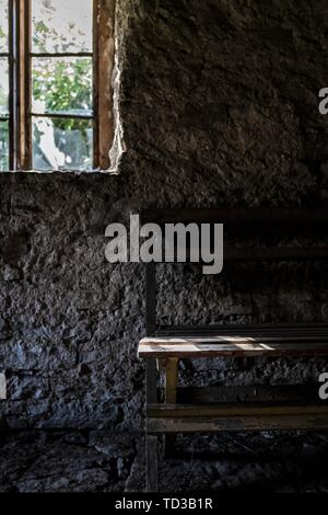 Interno di una vecchia casa in pietra con una finestra e. un lato di panca in legno fatta a mano Foto Stock