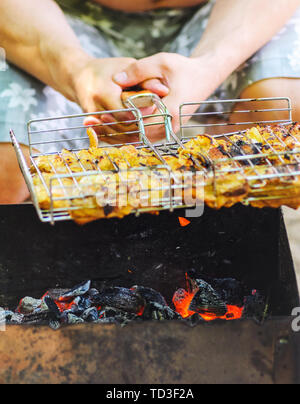 Man mano tenere la griglia del grill con carne di pollo su carbone caldo Foto Stock