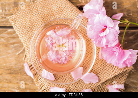 Fiore di Ciliegio The Cherry Blossom tè, una tazza di rosa fresca di fiori di ciliegio tè e fiori di ciliegio sul tavolo, guardando in giù verso la telecamera, freschi fiori di ciliegio e tè in vetro Foto Stock
