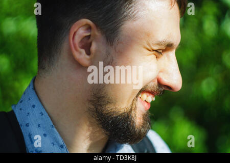 Ritratto di un allegro uomo sorridente contro il verde delle foglie degli alberi Foto Stock