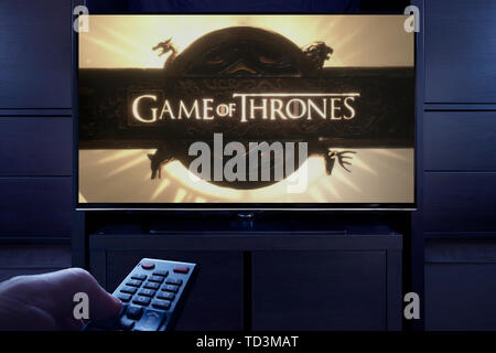 Un uomo punti un telecomando TV al televisore che visualizza il gioco dei troni a titolo principale schermo (solo uso editoriale). Foto Stock