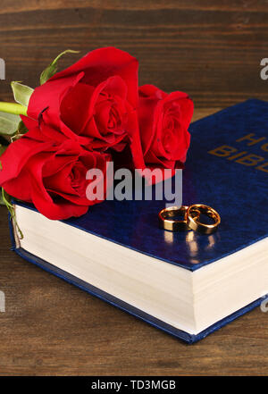 Gli anelli di nozze sulla bibbia con rose su sfondo di legno Foto Stock