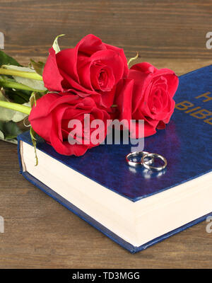 Gli anelli di nozze sulla bibbia con rose su sfondo di legno Foto Stock