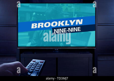 Un uomo punti un telecomando TV al televisore che visualizza il Brooklyn nove nove titolo principale schermo (solo uso editoriale). Foto Stock