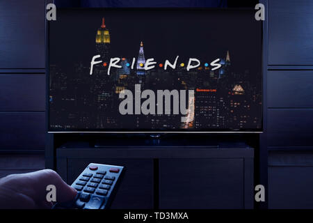 Un uomo punti un telecomando TV al televisore che visualizza gli amici titolo principale schermo (solo uso editoriale). Foto Stock