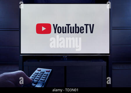 Un uomo punti un telecomando TV al televisore che visualizza il logo di YouTube TV on demand video streaming service (solo uso editoriale). Foto Stock
