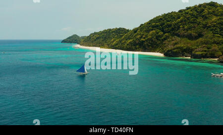 Sailing yacht in crystal turchesi acque cristalline proprio accanto alla spiaggia di sabbia bianca di isola tropicale, vista aerea. Barca a vela scivola sulle onde, Boracay, Filippine. Foto Stock