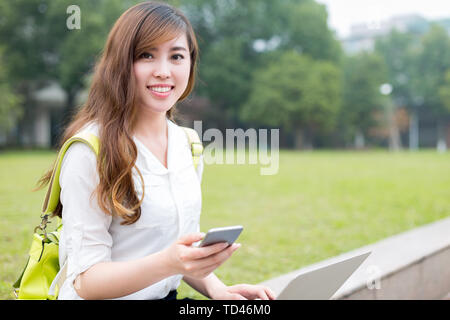 Asian bellissima femmina studen utilizzando il telefono cellulare nel campus Foto Stock