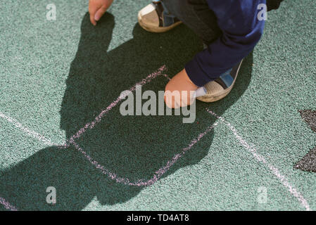 Bambino disegna con il gesso sulla strada. Rivestimento speciale per il disegno sul parco giochi. Il bambino disegna con un gessetto su un rivestimento in gomma di un bambini pla Foto Stock