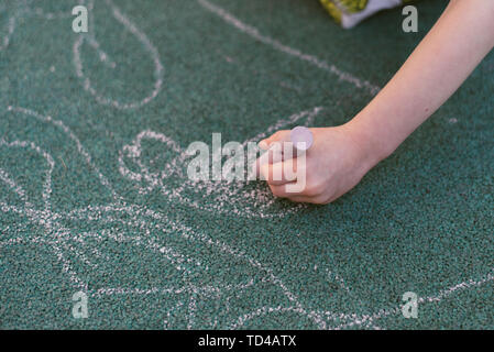 Bambino disegna con il gesso sulla strada. Rivestimento speciale per il disegno sul parco giochi. Il bambino disegna con un gessetto su un rivestimento in gomma di un bambini pla Foto Stock