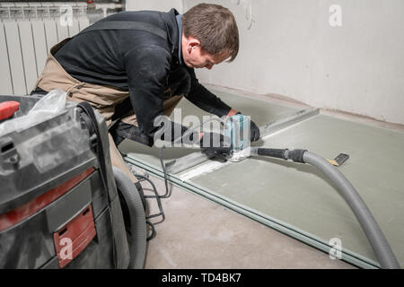 Lavoratore è utilizzando un edificio tool, utensili di fresatura e un aspirapolvere. muro a secco a novanta gradi. Foto Stock