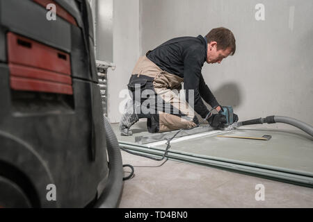 Lavoratore è utilizzando un edificio tool, utensili di fresatura e un aspirapolvere. muro a secco a novanta gradi. Foto Stock