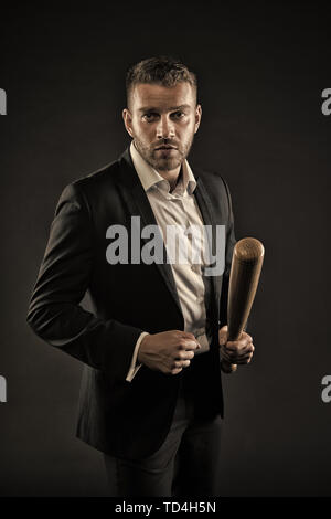Imprenditore o un uomo in abito formale su sfondo scuro. Uomo sulla faccia di rigorosa in posa con la mazza di legno. Aggressivo il concetto di business. Uomo con setola guarda fiducioso e minaccioso. Foto Stock
