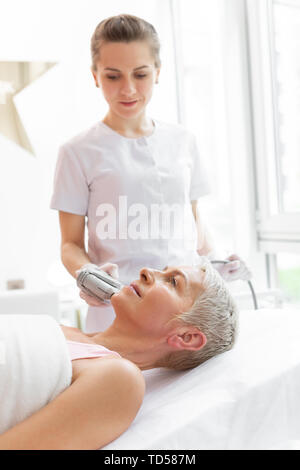 Durante il lavoro. Bella esperto cosmetologo guardando i suoi clienti volto mentre è in corso una procedura di bellezza Foto Stock