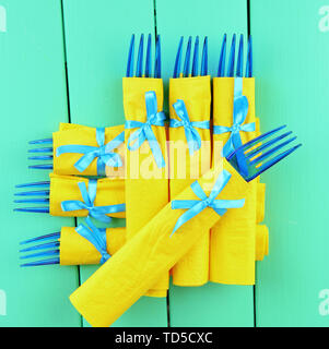 Il blu delle forcelle di plastica avvolto in carta gialla di tovaglioli, il colore di sfondo di legno Foto Stock